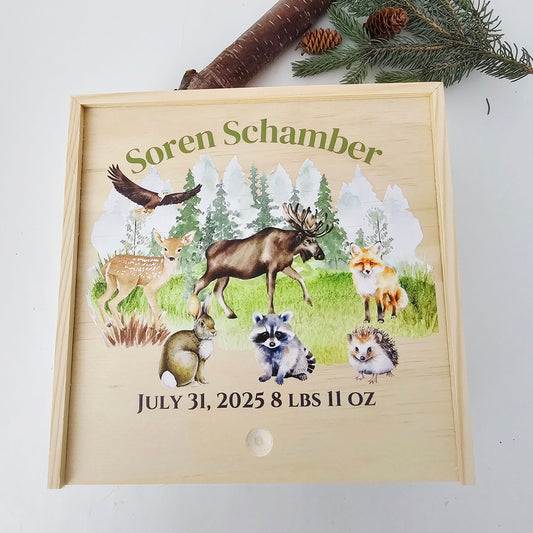 Personalized wooden baby birth announcement box featuring watercolor forest animals including a moose, fox, and eagle against a mountain backdrop.