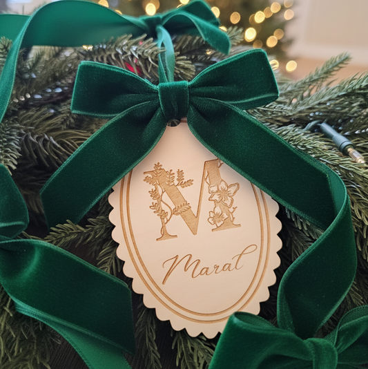 Decorative ornament with green velvet ribbon and gold tag on a Christmas tree.