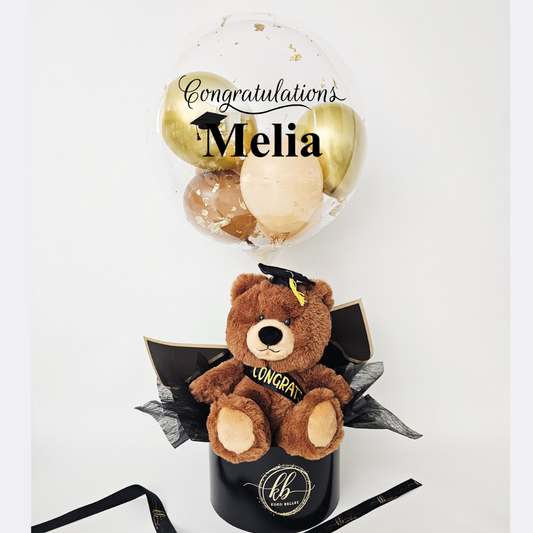 Graduation-themed teddy bear with balloons and a black box