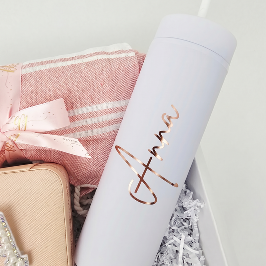 Close-up of a matte white skinny tumbler personalized with the name Anna in rose gold script vinyl lettering, nestled inside a pink-themed customized bridesmaid gift box.