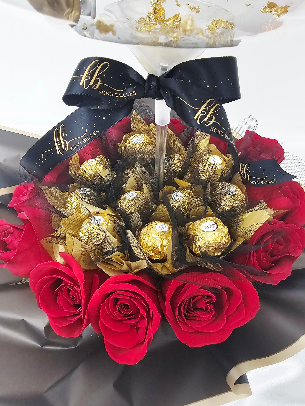 Custom birthday bubble balloon gift box with red roses, Ferrero Rocher chocolates, and gold and silver balloon arrangement.