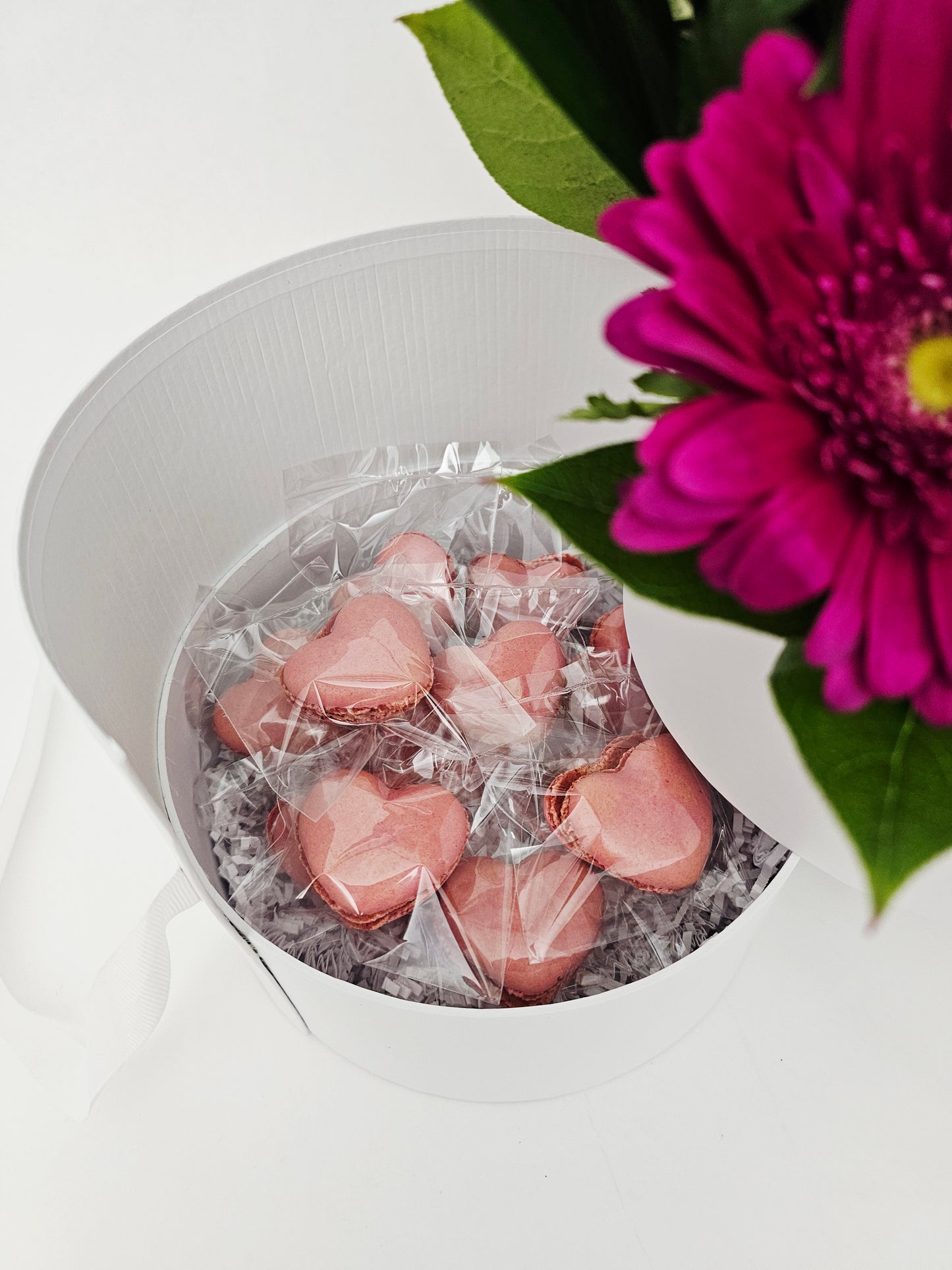 Pink heart-shaped Macarons in a white box with a purple flower on a white background