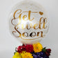 Clear balloon with gold text 'Get Well Soon' next to a bouquet of flowers on a white background