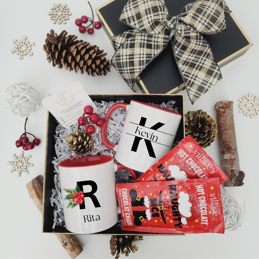 Gift set with personalized mugs and hot chocolate packets on a decorative surface.