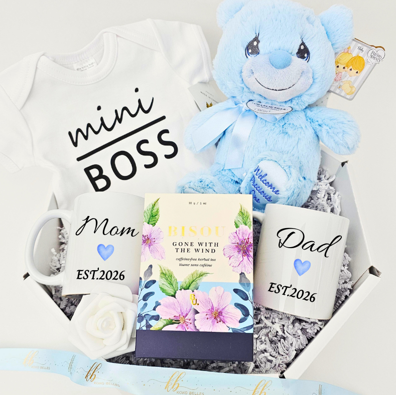 Gift set with baby-themed items including a blue teddy bear, baby onesie, mug, and Gourmet tea.