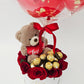 A white gift box arrangement featuring red roses, Ferrero Rocher chocolates, and a plush teddy bear holding a heart, topped with a clear bubble balloon reading "My Forever Valentine" filled with mini red balloons.