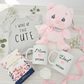 Baby-themed items including a pink plush toy, baby onesie, mugs for 'Mom' and 'Dad', and a box of gourmet tea.