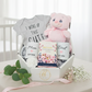 Baby gift set with onesie, mug, teddy bear, and a tea in a box on a white surface.
