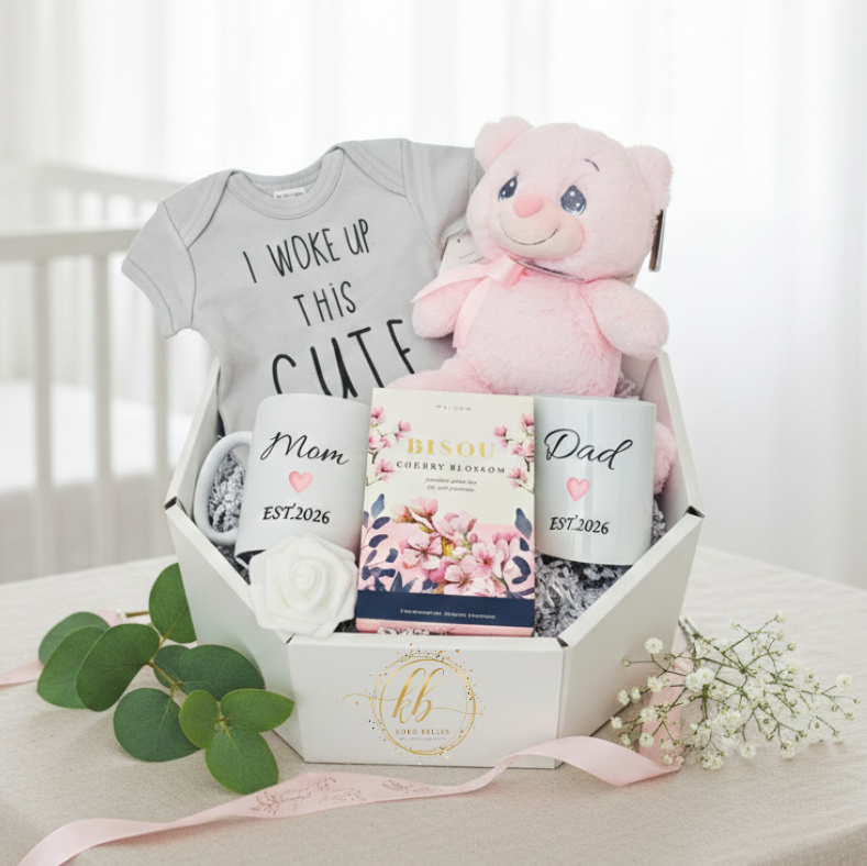Baby gift set with onesie, mug, teddy bear, and a tea in a box on a white surface.