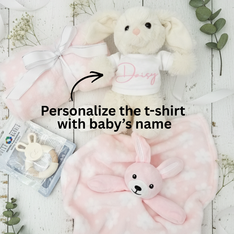 Baby gift set with plush toys and a t-shirt on a light wooden surface.
