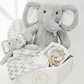 Gray plush elephant toy with a baby blanket and teething ring on a white background