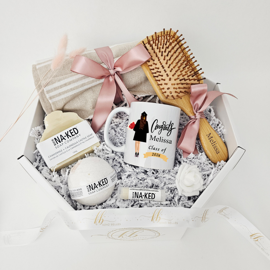 High-end graduation gift hamper featuring a personalized "Class of 2026" mug with a custom graduate illustration and the name Melissa, beautifully arranged with a llinen beach owel, an engraved wooden hair brush, and premium natural skincare items.