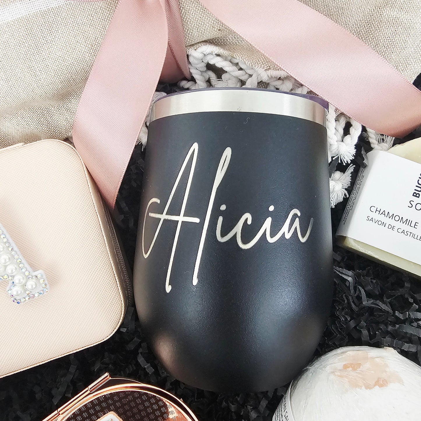 Close-up of a custom matte black insulated wine tumbler with an elegant script vinyl name inside a premium black and blush pink spa care package.