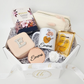 A customized women's spa and tea gift basket featuring a minimalist abstract floral mug personalized for Emma. The luxury white octagonal box is filled with white crinkle paper, holding a premium box of Bisou Houjicha tea, a cream makeup bag, a pearl initial case, an engraved rose gold mirror, and gold eye masks.