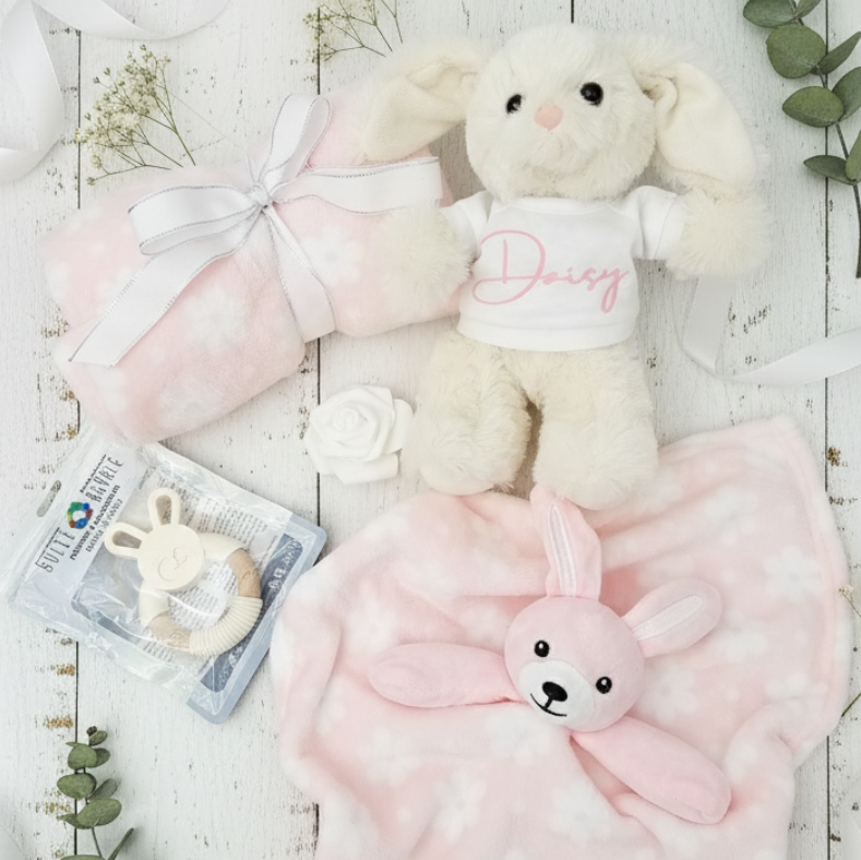 Baby gift set with plush bunny, blanket, and toys on a light wooden surface.