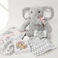 Gray elephant plush toy with a baby rattle and blanket on a white background