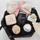 A luxury black octagonal gift box featuring a personalized matte black wine tumbler with the name Alicia in script, a blush pink initial travel jewelry case, a matching compact mirror, a beige Turkish towel, and Buck Naked soap products.