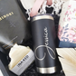 An elegant custom wellness gift package for her featuring a permanently laser-etched black insulated travel tumbler, artisanal bath salts, natural camomile soap, and a dried palm fan accent over black crinkle paper.