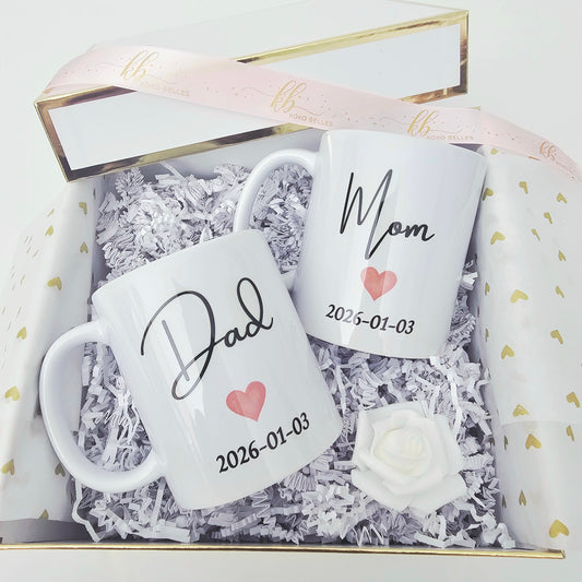 Two white mugs with 'Dad' and 'Mom' and dates in a decorative box.