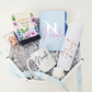 A luxury white octagonal gift box curated with a light blue custom Nicole notebook, a personalized matte white skinny tumbler in rose gold vinyl, a white ceramic coffee mug with a black name and pink heart, Bisou loose leaf tea, and a rose gold pineapple tea infuser.