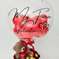 Boîte-cadeau de Saint-Valentin comprenant des roses rouges, des chocolats Ferrero Rocher et un ourson en peluche, surmontée d'un ballon bulle transparent personnalisé « My Forever Valentine ».